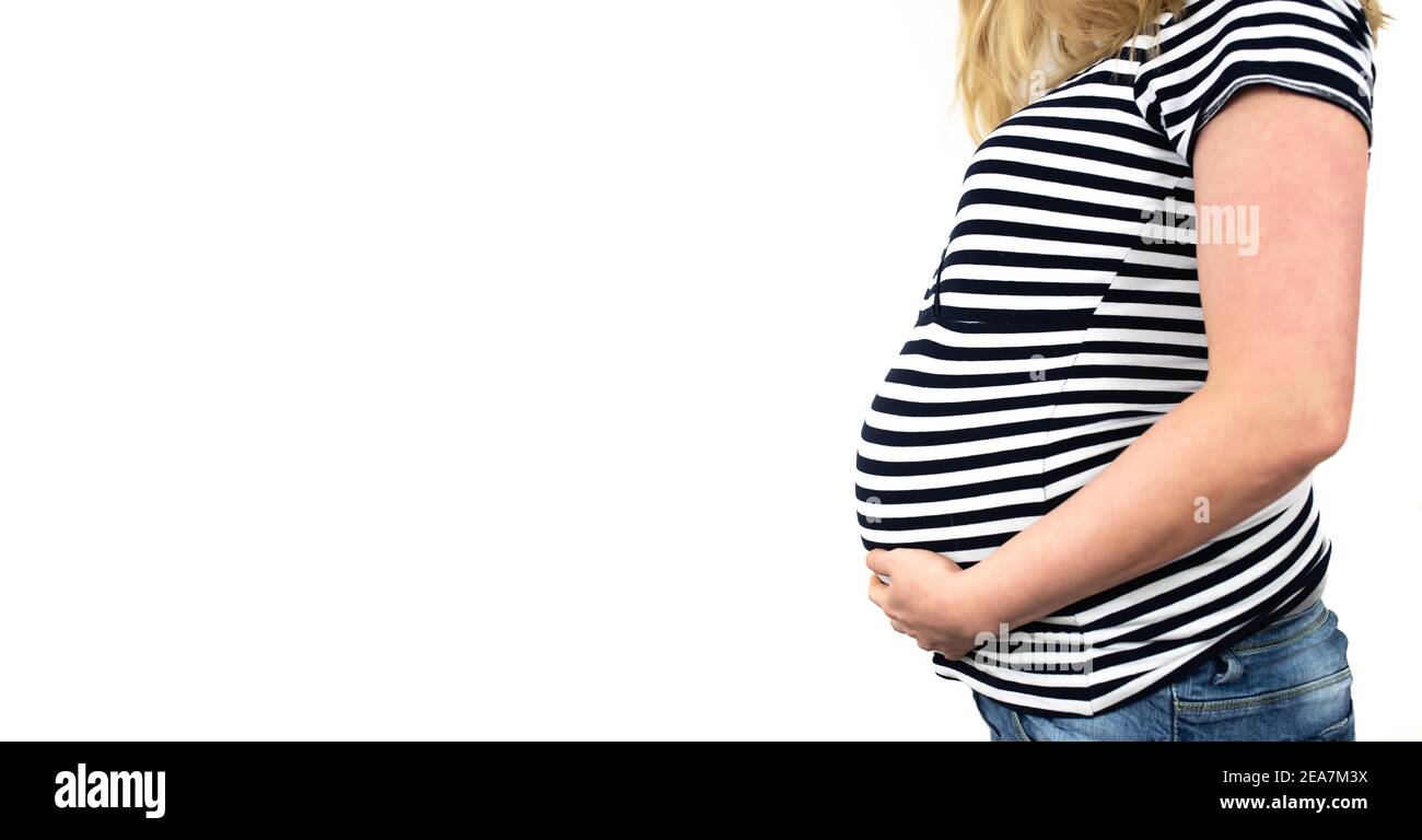 vue latérale de la section médiane de la femme enceinte de 9 mois haut rayé un jean avec les mains sur le ventre contre blanc arrière-plan Banque D'Images