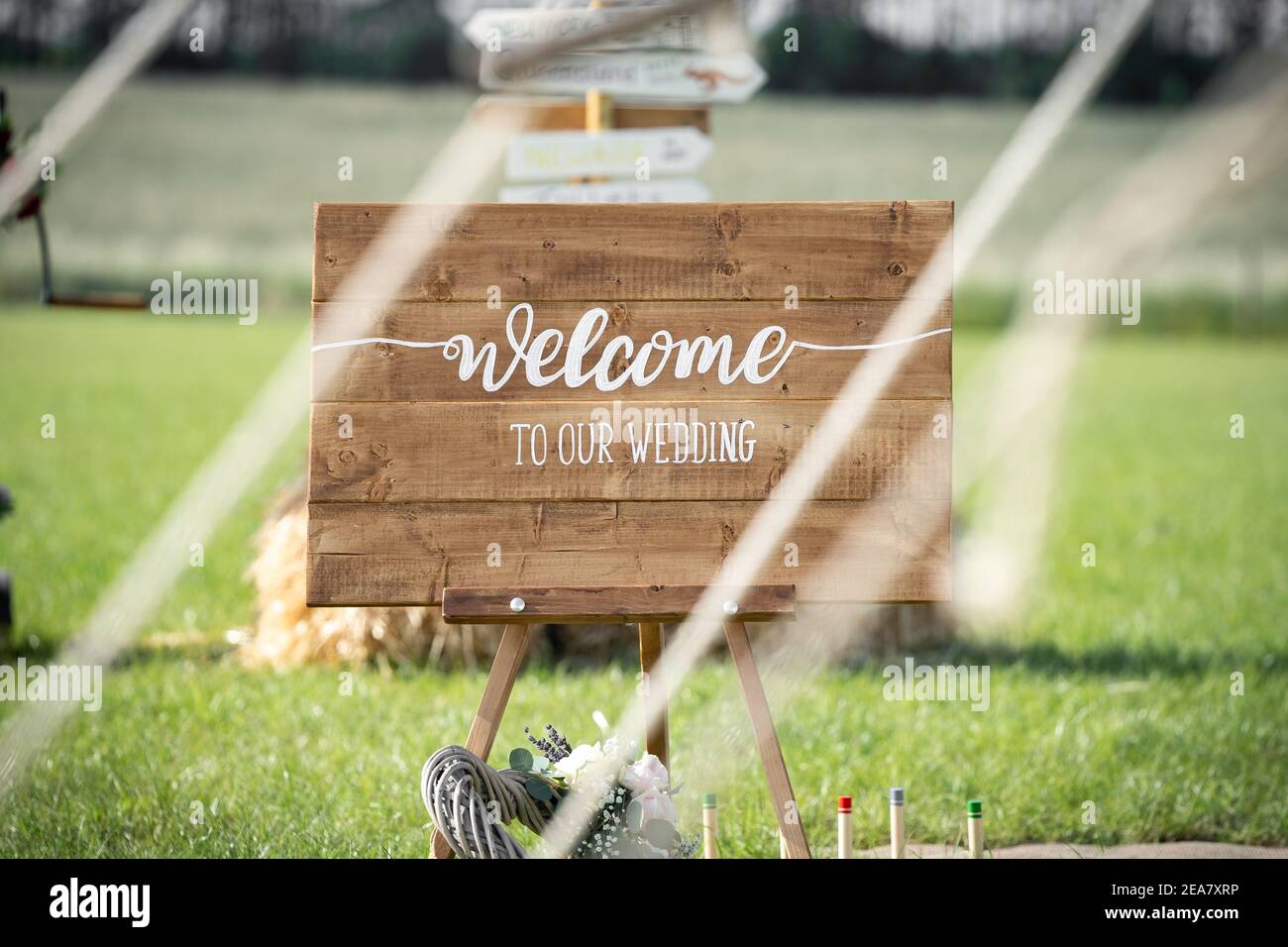 Bienvenue à notre mariage rustique panneau en bois peint à la main l'écriture à la ferme de mariage vu à travers des cordes de tente dessus journée d'été lumineuse avec les terres agricoles Banque D'Images
