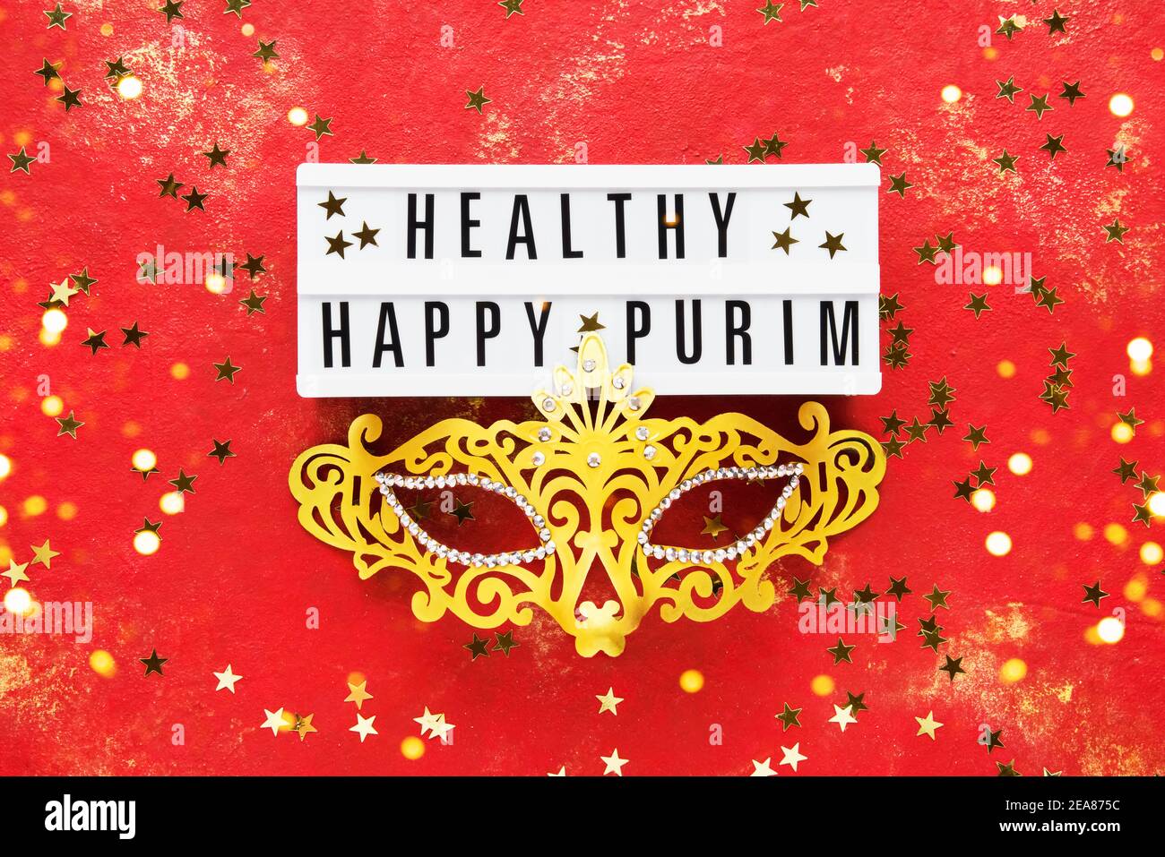 Masque de carnaval doré et étoiles dorées sur fond rouge. Vue de dessus, espace de copie. Concept de fête du Carnaval. Pose à plat Banque D'Images