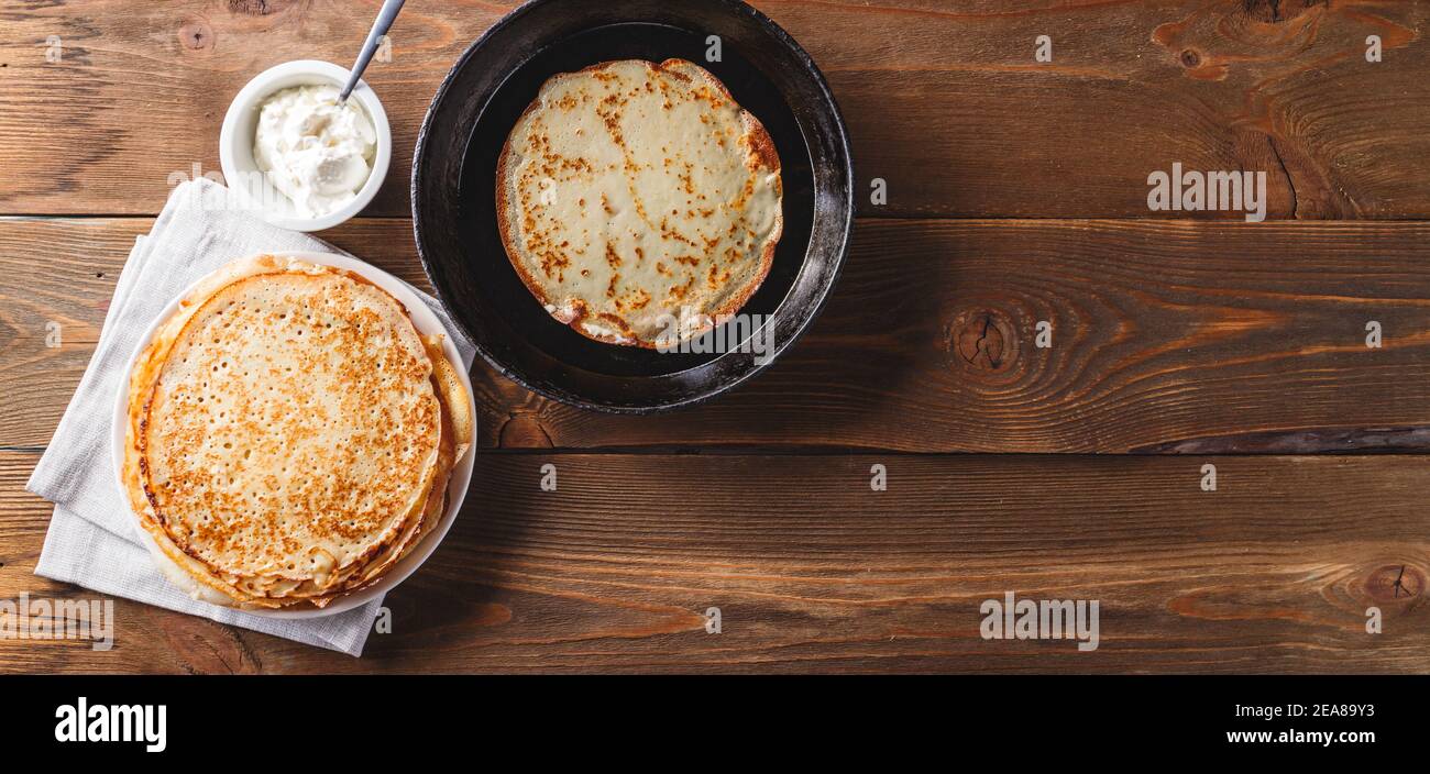 Crêpes russes traditionnelles Blini empilées dans une assiette et crêpes dans une poêle en fonte sur une table en bois. Repas du festival russe Maslenitsa. Kit russe Banque D'Images