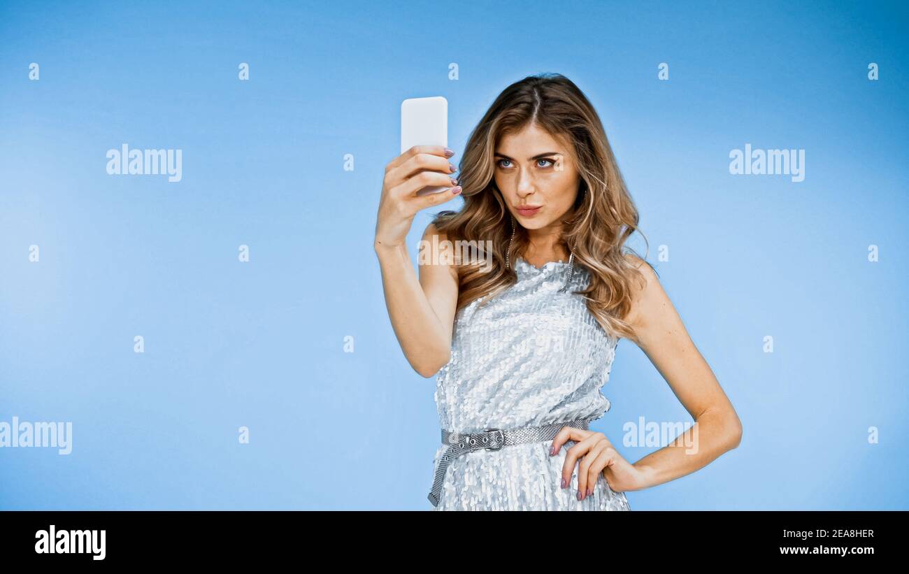 femme qui fait des pieds sur les lèvres tout en prenant le selfie et debout avec la main sur la hanche sur le bleu Banque D'Images