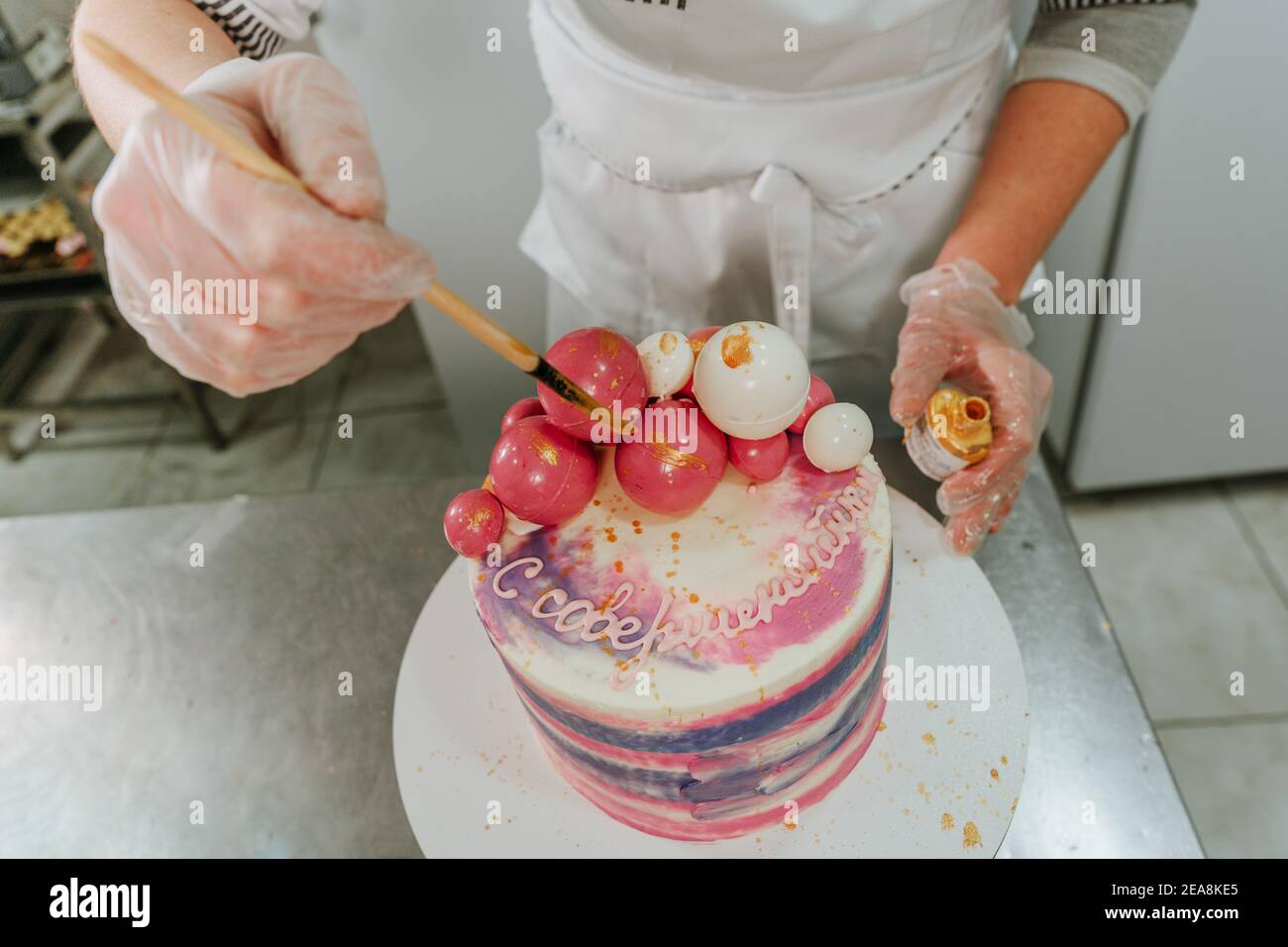 Gros plan de la confiserie féminine décorant le gâteau d'anniversaire à l'aide de comestible colorer et brosser d'or dans le studio de confiserie Banque D'Images