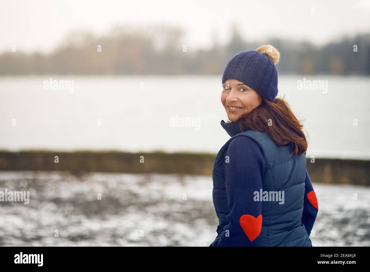 Bonne femme brune d'âge moyen en chandail avec chapeau en tricot tournant et regarder la caméra Banque D'Images