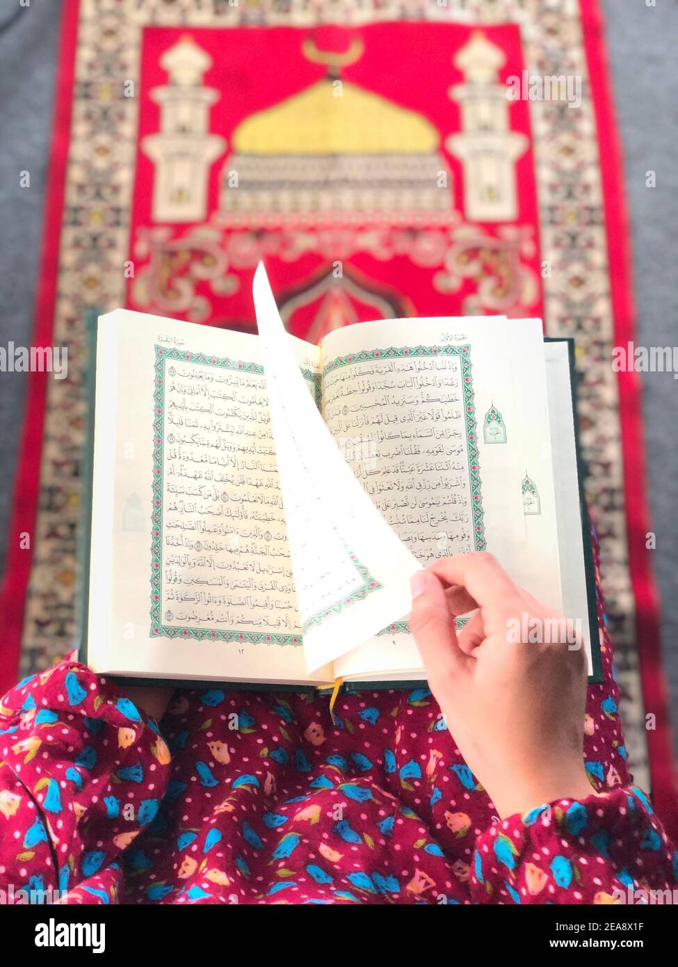 Une femme lisant le Coran sur un tapis de prière Banque D'Images