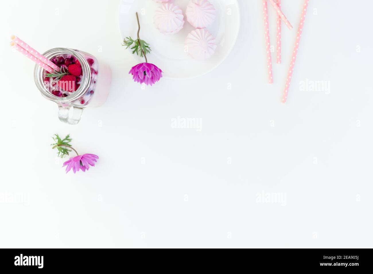 Délicieux smoothie aux baies avec pailles, guimauve et fleurs roses sur fond blanc. Pose à plat. Banque D'Images