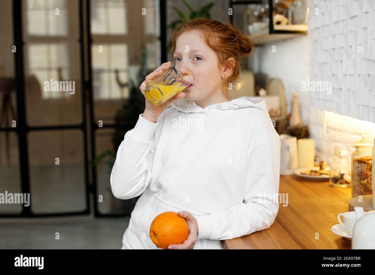 Une Jeune Fille Aux Cheveux Boucles Rouges Boit Du Jus D Orange Dans La Cuisine Des Aliments Sains Pour Bebe Photo Stock Alamy