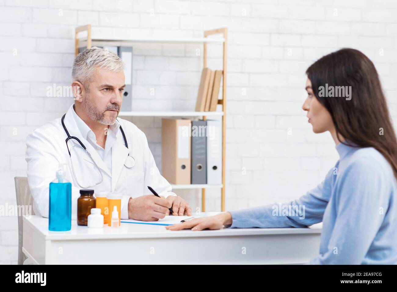 Un homme âgé sérieux, au pelage blanc, écoute la patiente et prend des notes à la table Banque D'Images
