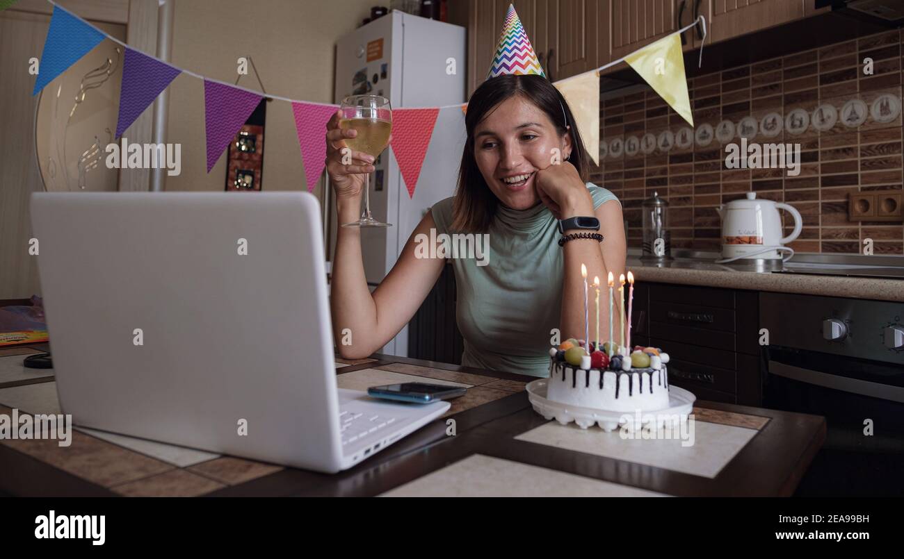 Femme célébrant son anniversaire par vidéo appel de fête virtuelle avec des amis. Ses coups et sa bougie. Lieu de travail maison décoré authentique. Coronavir Banque D'Images