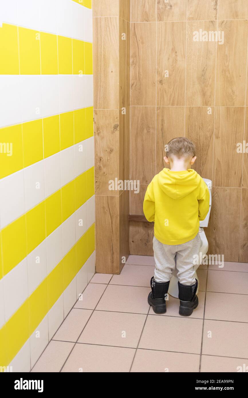 Enfant garçon enfant pising dans cuvette de toilette dans les toilettes d'enfants avec tuiles jaunes. Concept d'hygiène dans les lieux publics. Banque D'Images