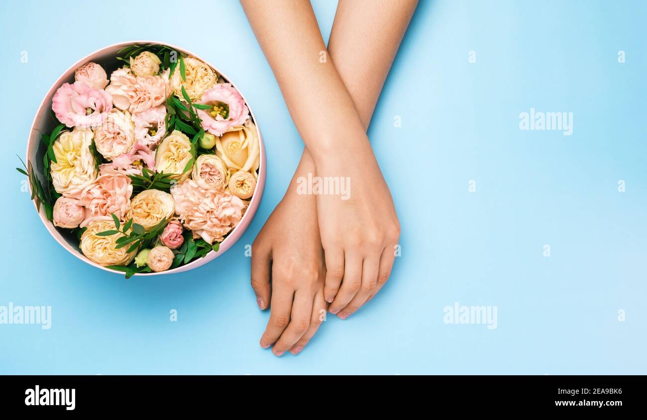 Boîte avec de belles fleurs à côté des mains de womans sur le fond bleu avec espace de copie. Concept de carte salone beauté. Cadeau pour le 8 mars, Fête des mères Banque D'Images