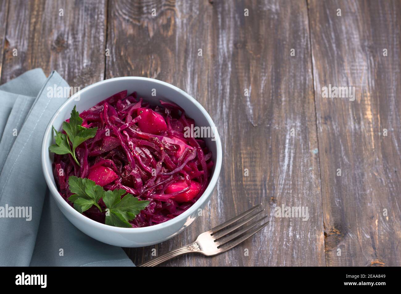 Ragoût de chou rouge avec des pommes, des épices et des légumes verts sur fond de bois, carré, espace libre. Délicieux aliments sains faits maison Banque D'Images