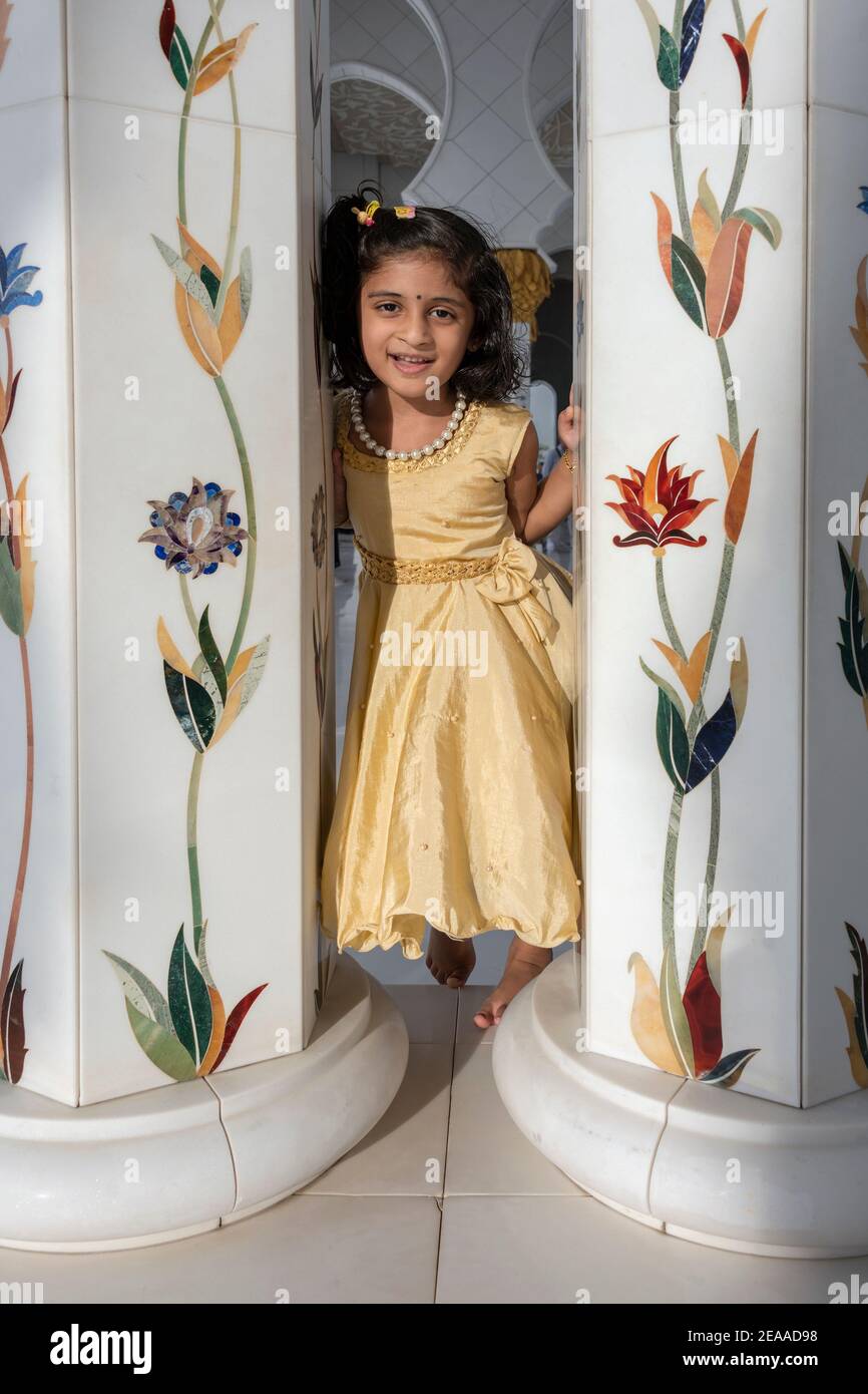 Fille souriante dans une robe dorée entre deux colonnes en mosaïque, Grande Mosquée Sheikh Zayed, Abu Dhabi, Émirats Arabes Unis Banque D'Images
