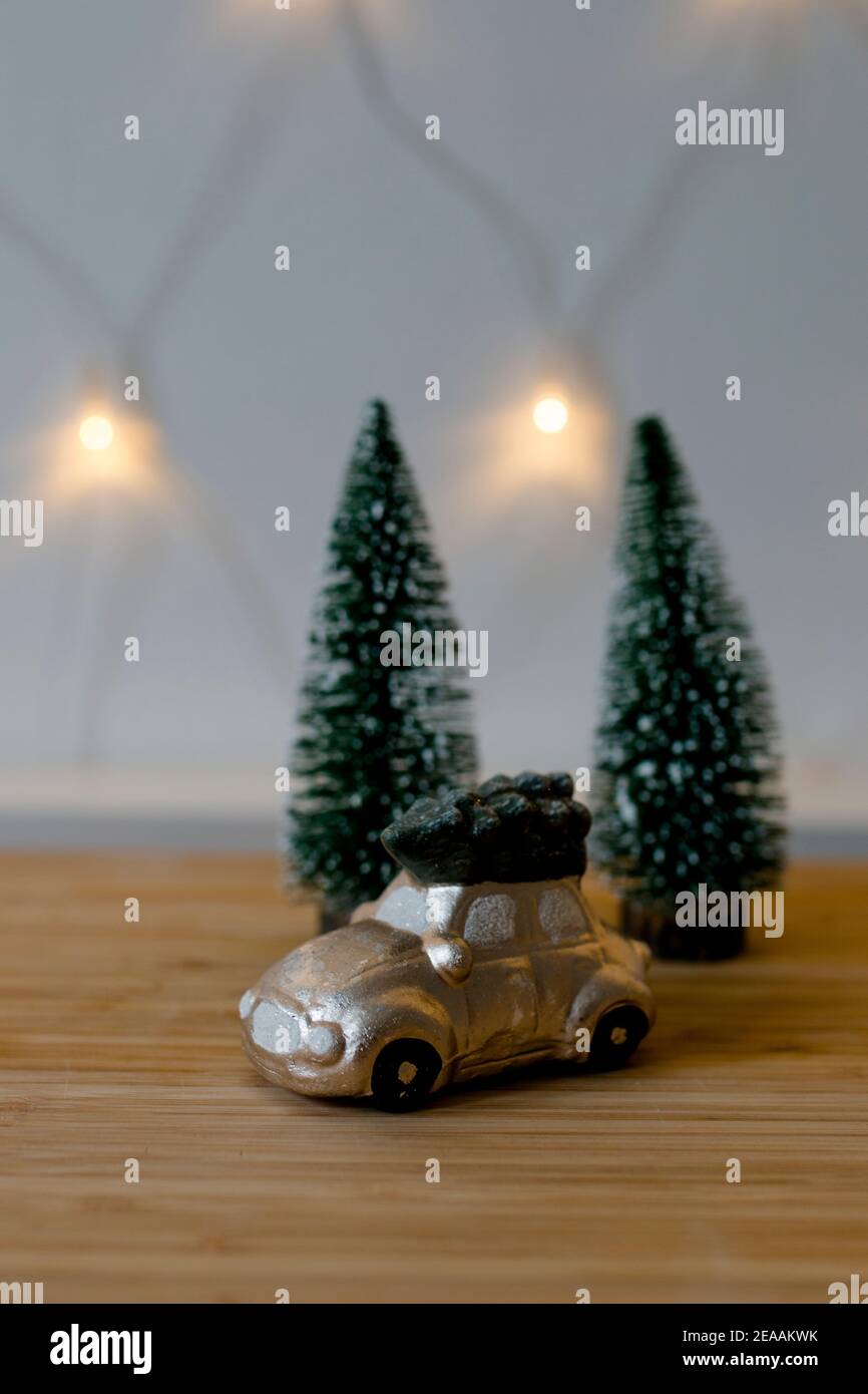 Encore la vie, petite voiture dorée avec un sapin sur le toit en face de sapins et une chaîne de lumières, romantique humeur de Noël Banque D'Images