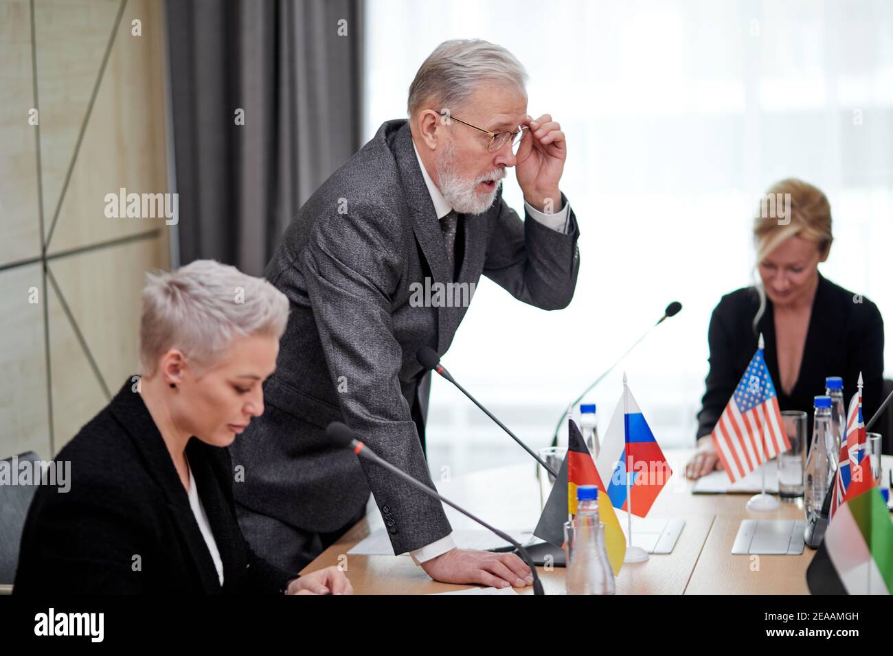 un homme politique senior offre son plan d'action et partage son opinion, un homme âgé en costume s'adressant à un groupe multiethnique de partenaires assis à son bureau en conseil d'administration Banque D'Images