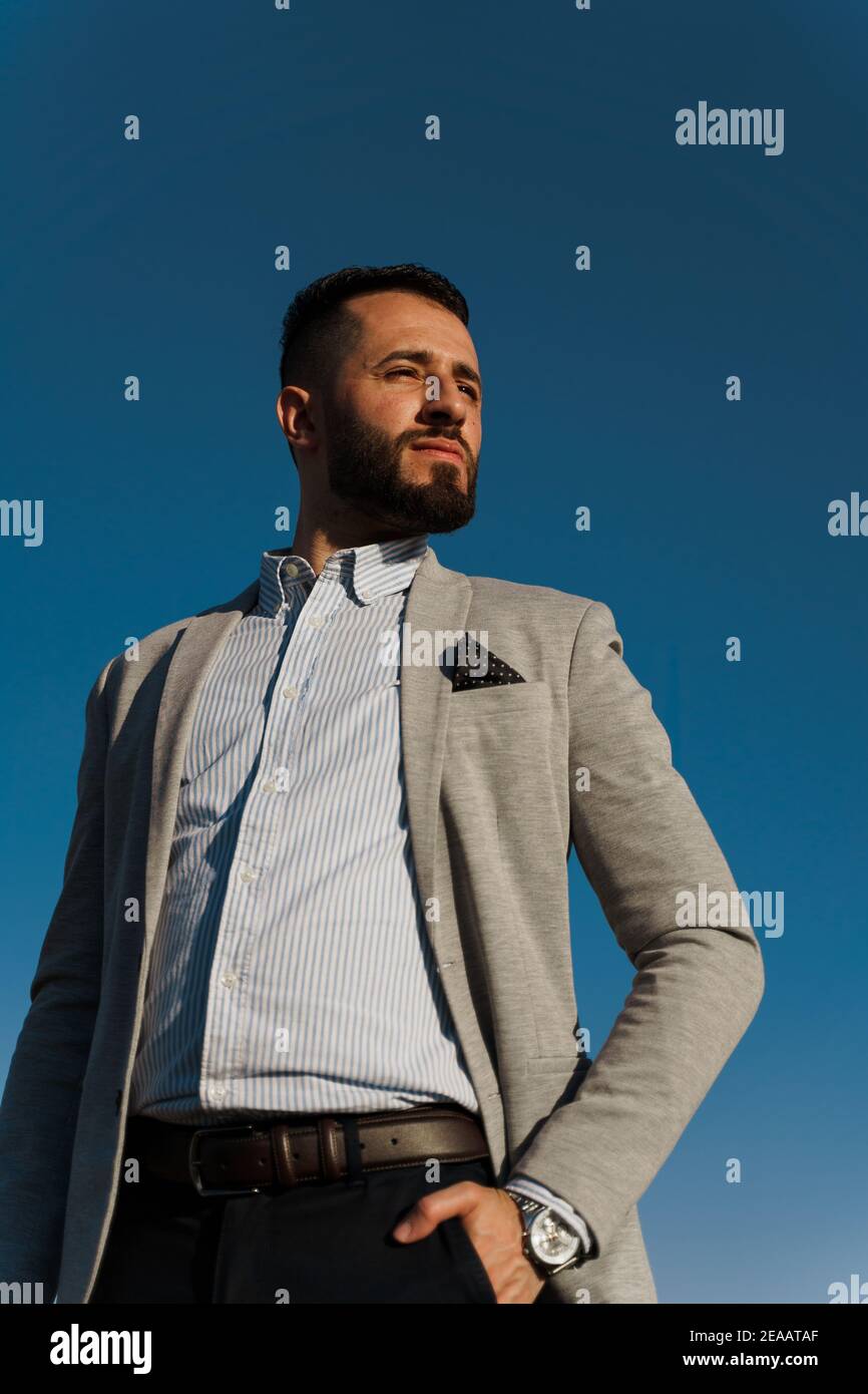 Bel homme arabe barbu dans des lunettes de soleil sur fond bleu ciel. Homme d'affaires musulman confiant. L'homme arabe a pleuré dans un manteau gris Banque D'Images