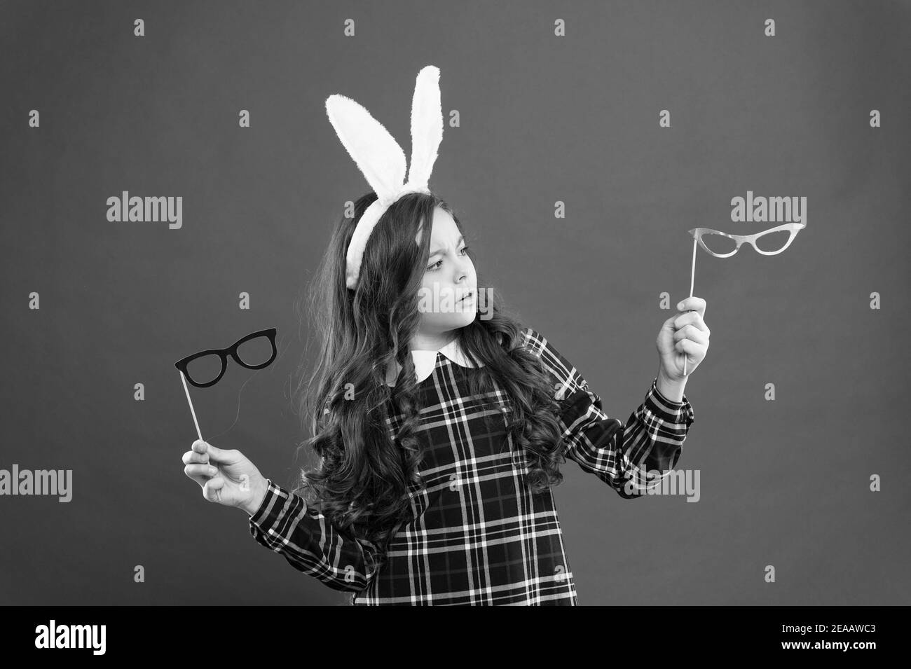 C'est un choix difficile. Joyeuses pâques. Les petites filles portent des oursons de lapin le jour de Pâques. Les enfants sérieux choisissent des lunettes de fête. Lapin de Pâques avec oreilles. Enfant adolescent en costume de lapin s'amuser. Banque D'Images