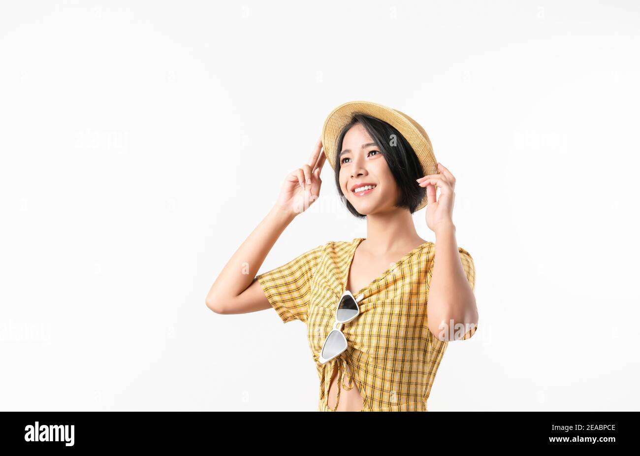 Photo studio de belle femme asiatique gaie dans une robe jaune et portant un chapeau et un stand sur fond blanc. Banque D'Images