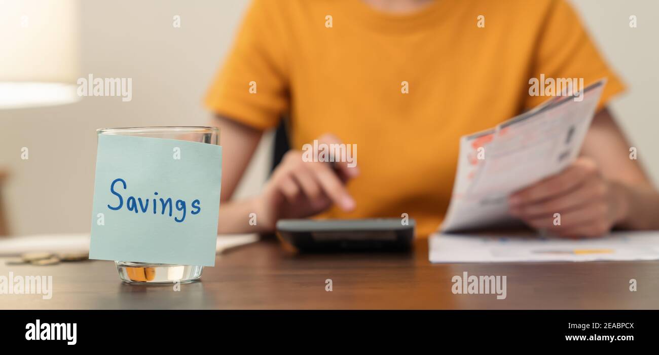 Sauver le papier-note collé sur la bouteille avec des pièces à l'intérieur, la jeune femme utilise une calculatrice et le plan de revenu et de dépenses divisées par catégories. Banque D'Images