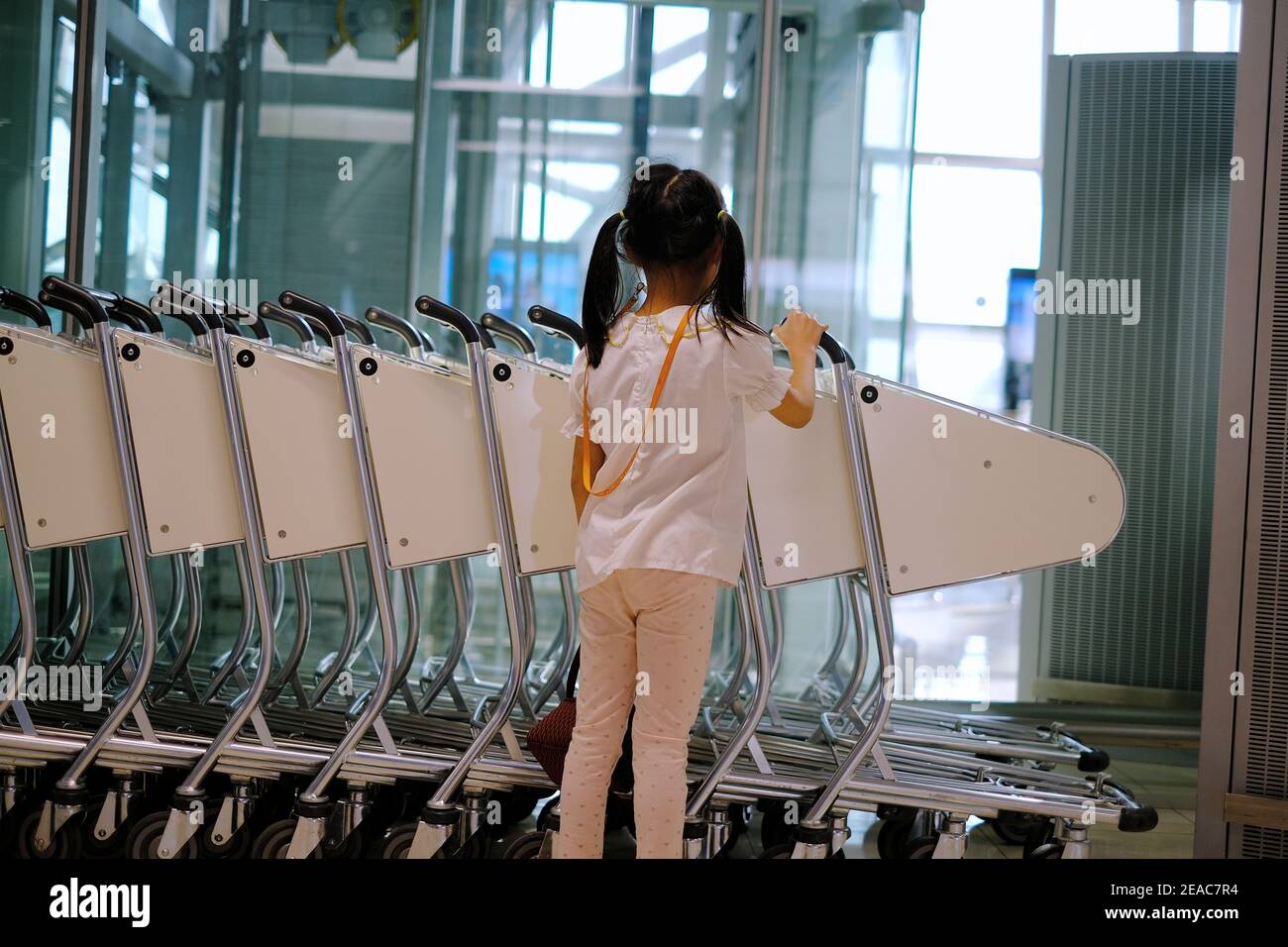 La vue arrière d'une jolie jeune fille asiatique poussant un chariot à un terminal de l'aéroport pour transporter ses bagages à sa porte avant son vol. Banque D'Images