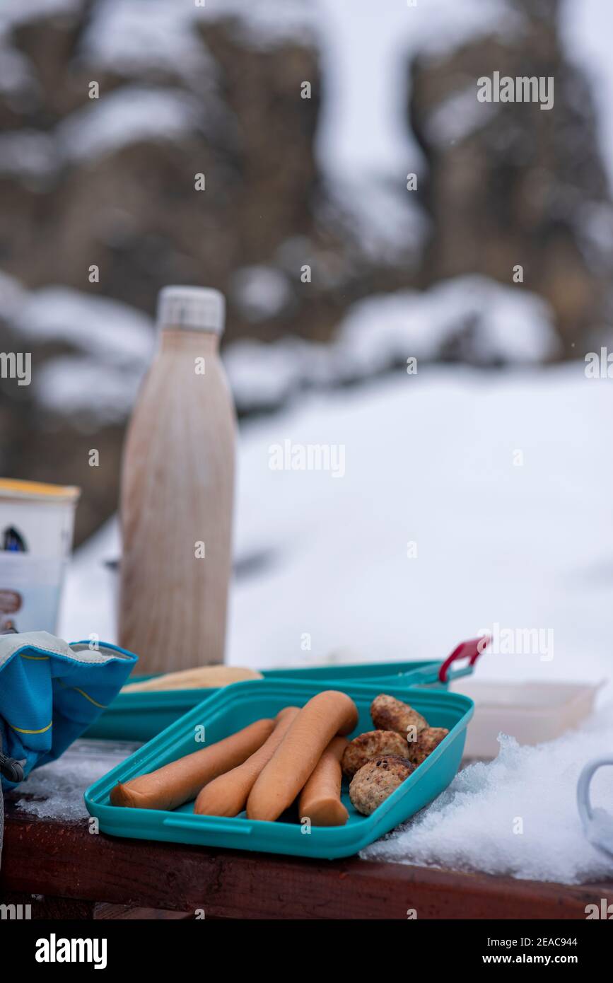 Pique-nique en hiver, les saucisses sont posées sur une table dans une boîte de Tupperware. Il y a un thermos à côté. Banque D'Images
