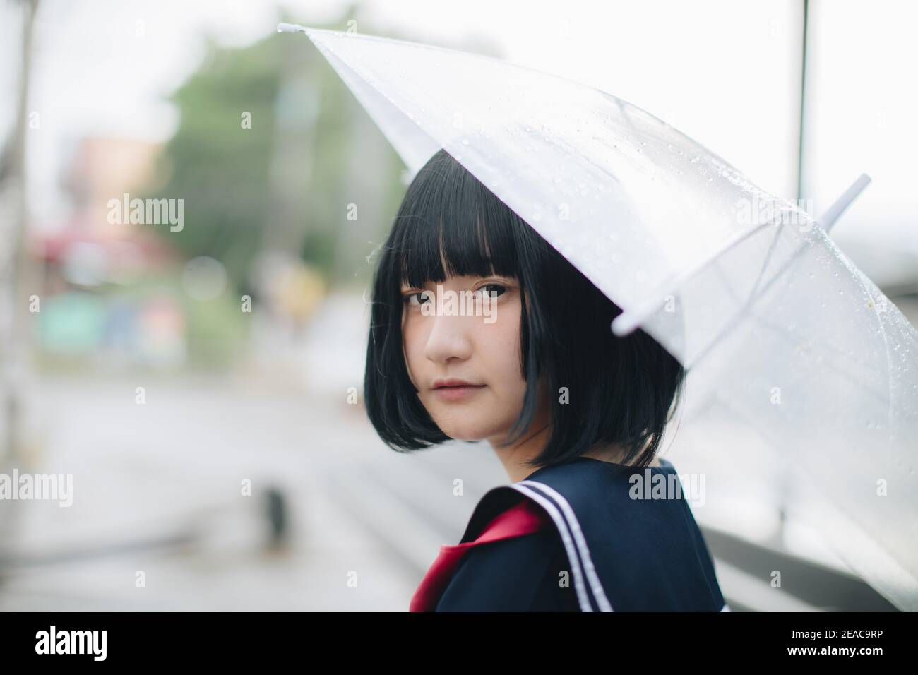 Fille d'école asiatique à la recherche avec parapluie dans la ville urbaine Banque D'Images