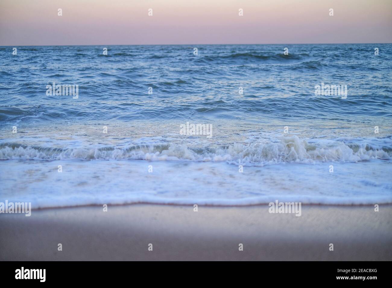 Une photo d'un vase vue sur la mer depuis le bord d'une plage juste avant le coucher du soleil avec lumière dorée dedans le ciel et l'eau de mer mousseuse comme il se débarque la plage de sable Banque D'Images