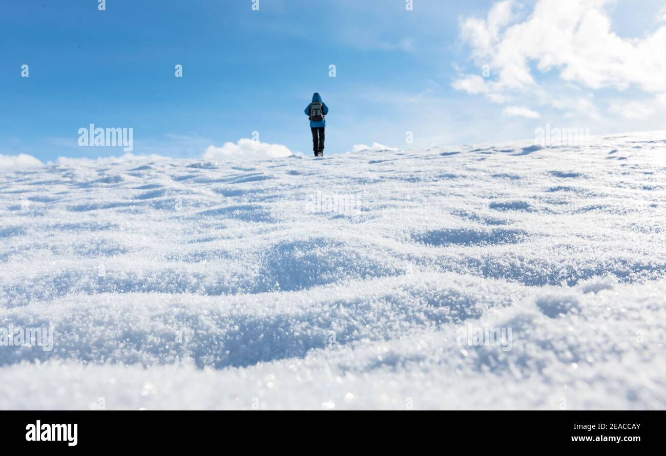 Une personne avec une veste bleue marche dans la neige l'arrière-plan Banque D'Images