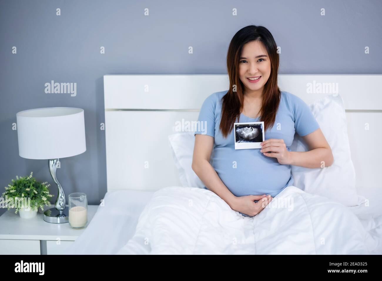 femme enceinte heureuse tenant une photo d'échographie sur un lit Banque D'Images