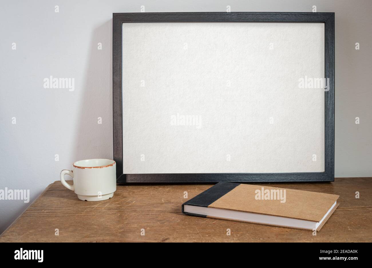 maquette de cadre noir, sur la vieille table et le mur blanc, avec un carnet à croquis ou un journal et une tasse à café. sur une table en bois. Banque D'Images