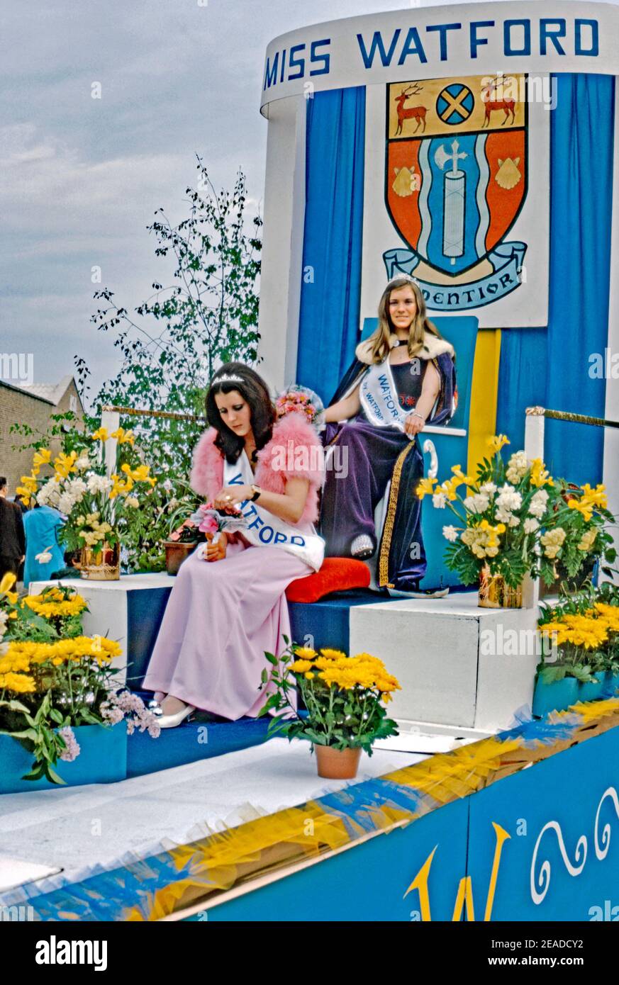 Un char de parade portant ‘miss Watford’ et sa femme d’honneur au défilé annuel du Carnaval de Whitsun, Watford, Hertfordshire, Angleterre, Royaume-Uni 1973. La femme est dans sa robe de cérémonie et porte la ceinture de sa gagnante. Derrière elle se cache le blason de Watford. La devise est «Audentior», signifiant «avec plus d'audace» (de Virgile Aeniad). Banque D'Images