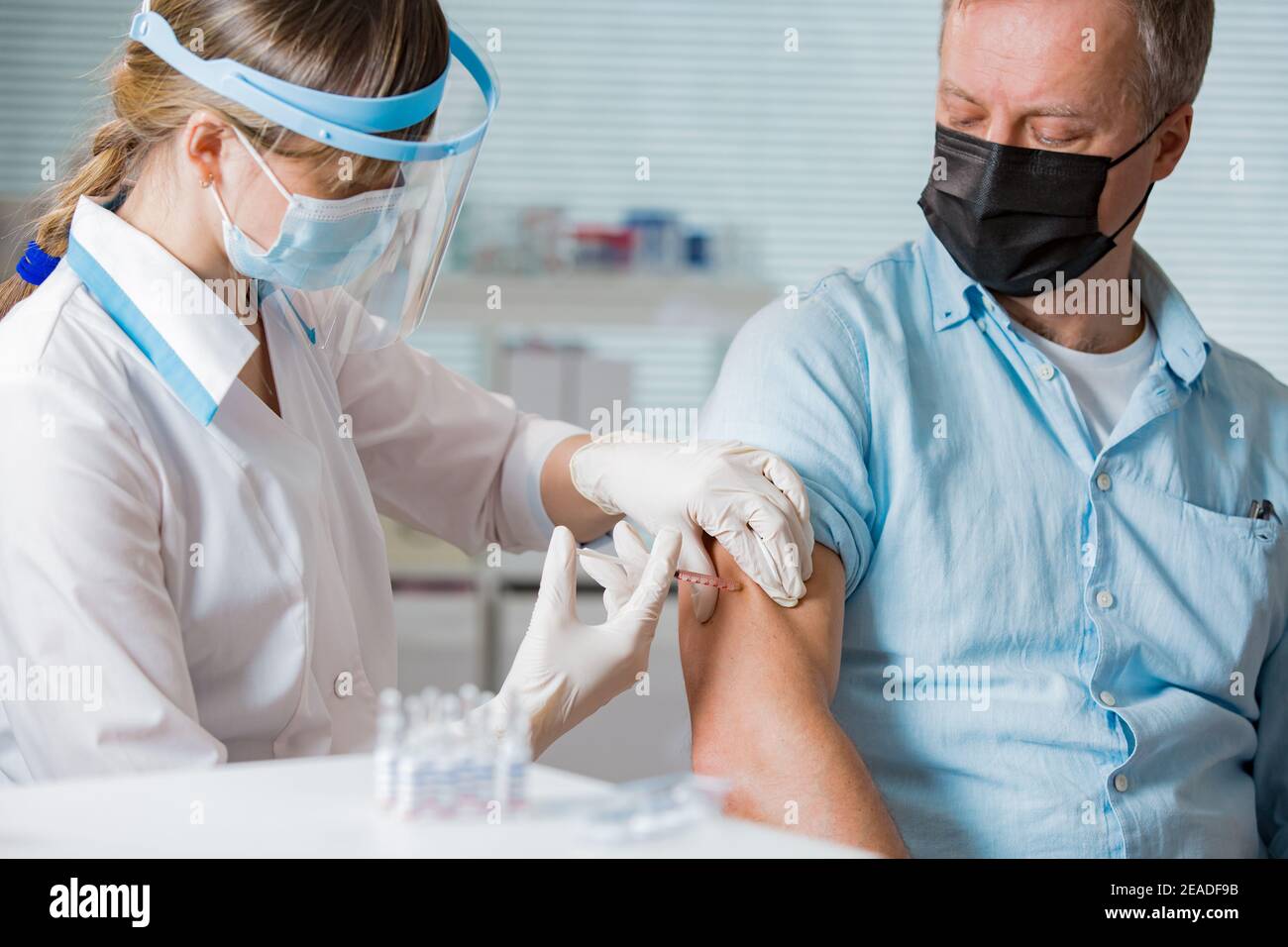 Femme médecin avec masque chirurgical et gants donnant l'injection du vaccin à l'homme à l'hôpital. Vaccination pendant la pandémie de COVID-19 Banque D'Images