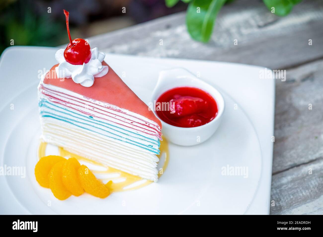 Gâteau à la crêpe arc-en-ciel et une cerise avec sauce fraise sur fond de table en bois. Banque D'Images