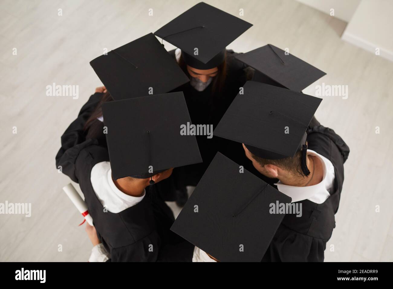 Groupe de diplômés dans les mortaboards debout à proximité dans cercle et s'embrasser Banque D'Images