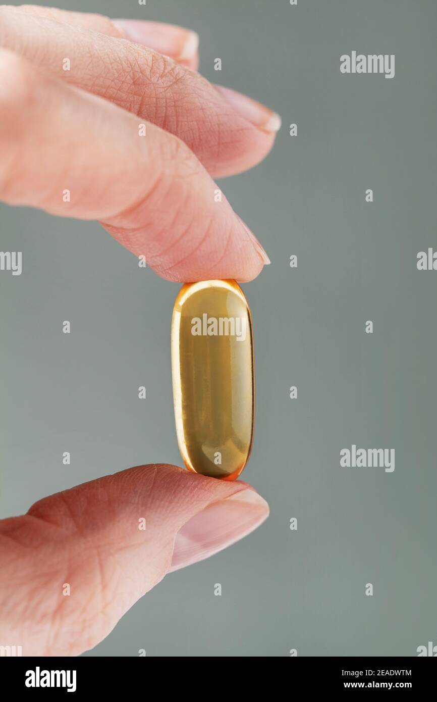 Main femelle tenant une grande capsule jaune de supplément nutritionnel . Supplément alimentaire, vitamine D, oméga, vitamine C, multivitamines Banque D'Images