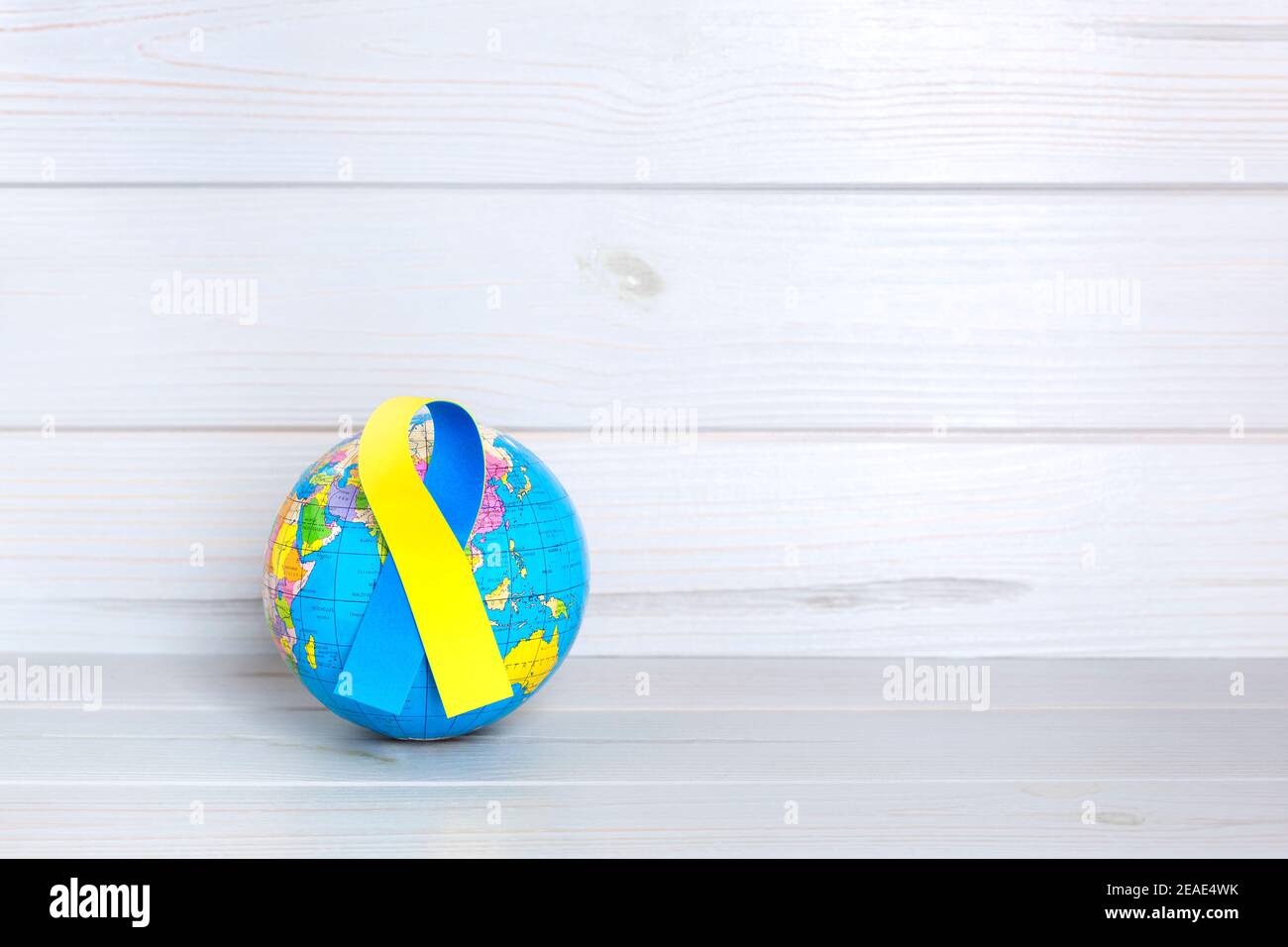 Globe terrestre avec ruban jaune et bleu sur fond en bois. Concept de la Journée mondiale du syndrome de Down. Espace pour le texte. Banque D'Images