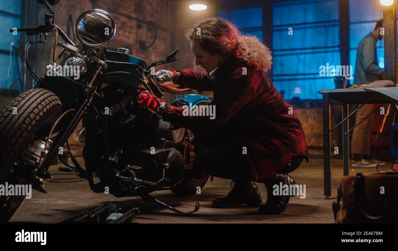 Jeune belle femme mécanicien est la fixation d'une moto Bobber personnalisée. Talentueuse fille portant une chemise à carreaux. Elle utilise une clé à cliquet. Créatif Banque D'Images