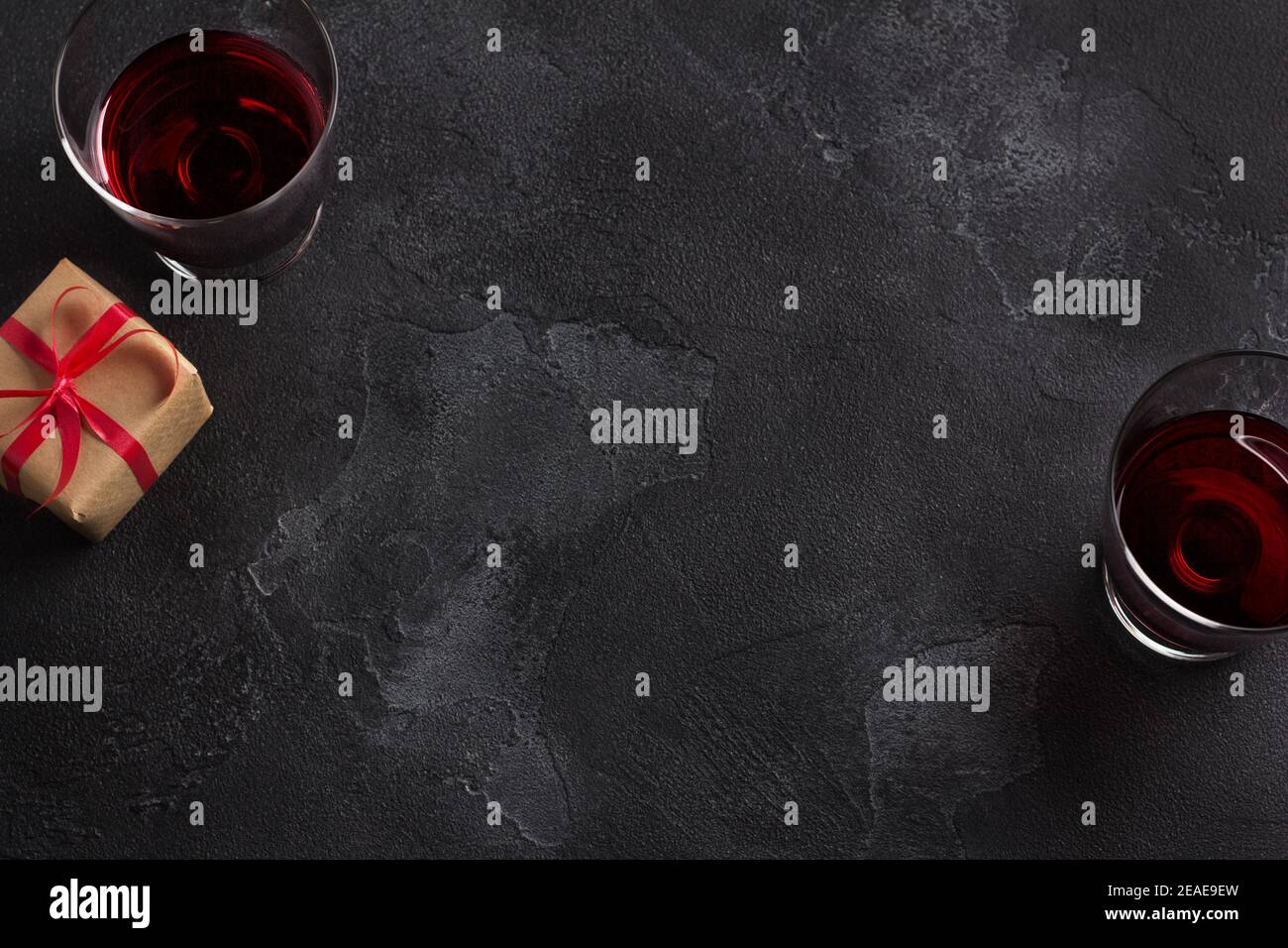 Arrière-plan noir avec deux verres de vin rouge et un cadeau en papier artisanal avec un ruban rouge, vue du dessus, espace copie Banque D'Images