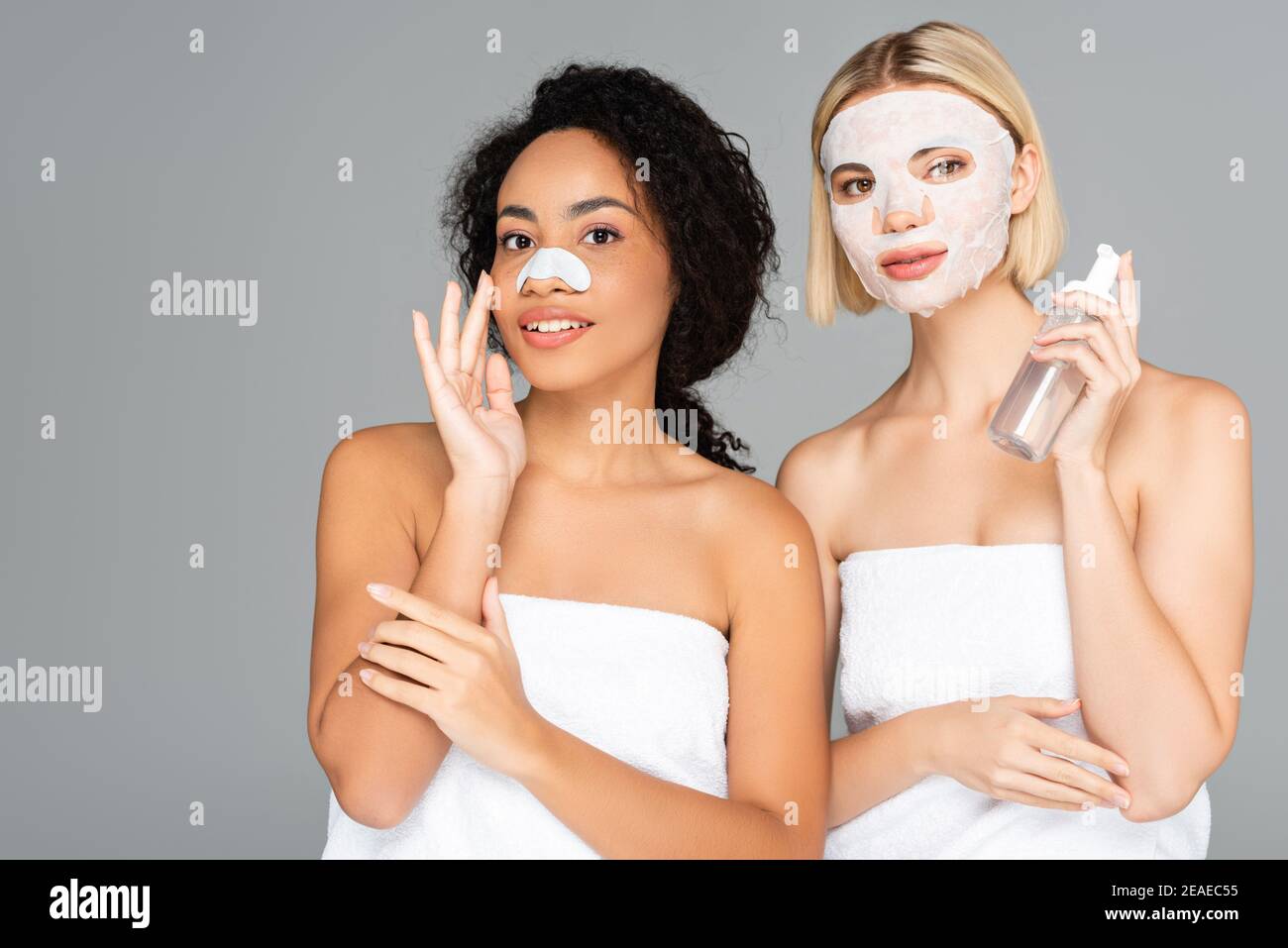 Femmes multiculturelles souriantes dans un masque en feuille et une tenue à rayures nettoyantes mousse isolée sur gris Banque D'Images