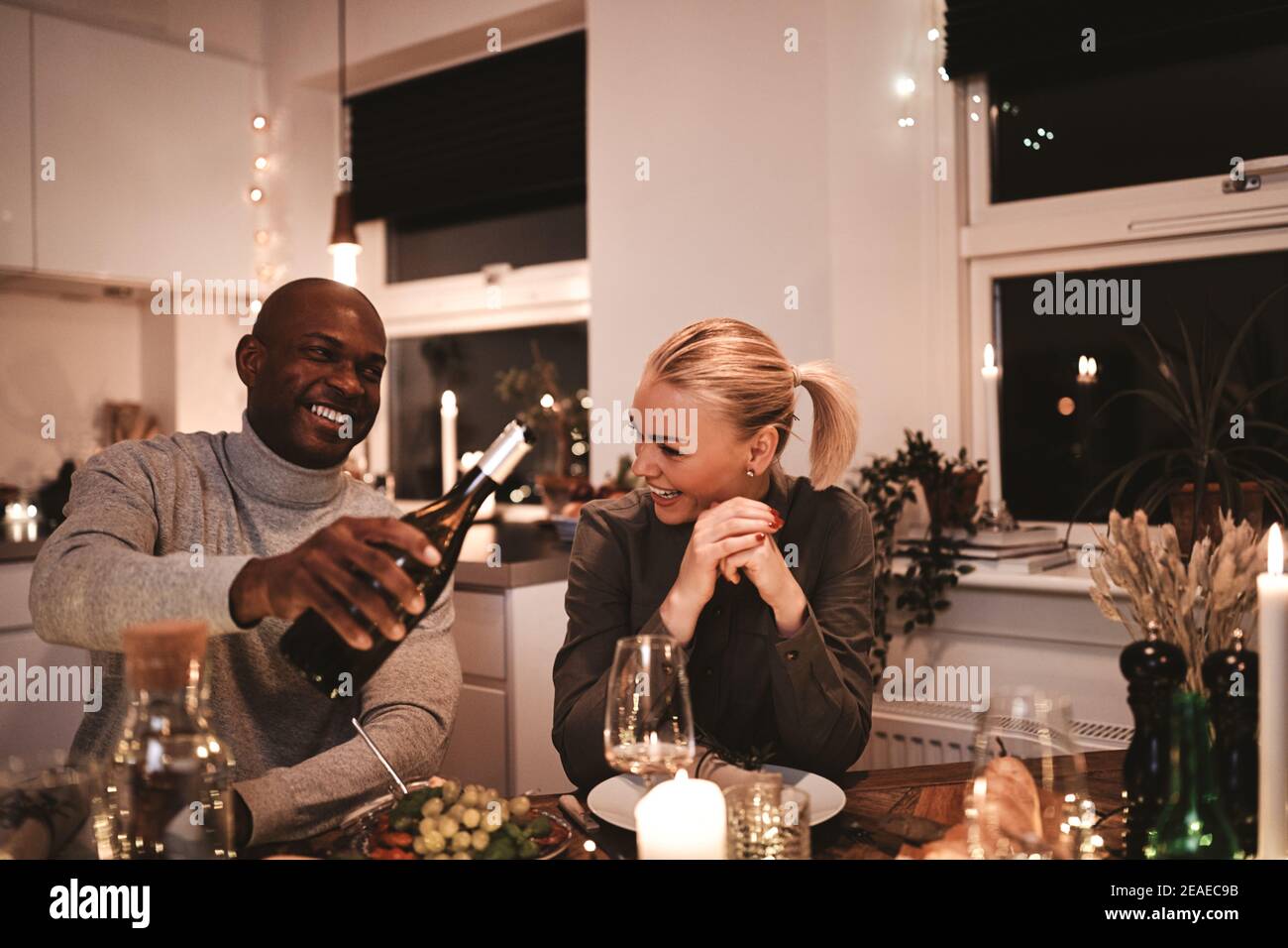 Rire homme versant son épouse un verre de vin pendant un dîner aux chandelles autour d'une table avec des amis Banque D'Images