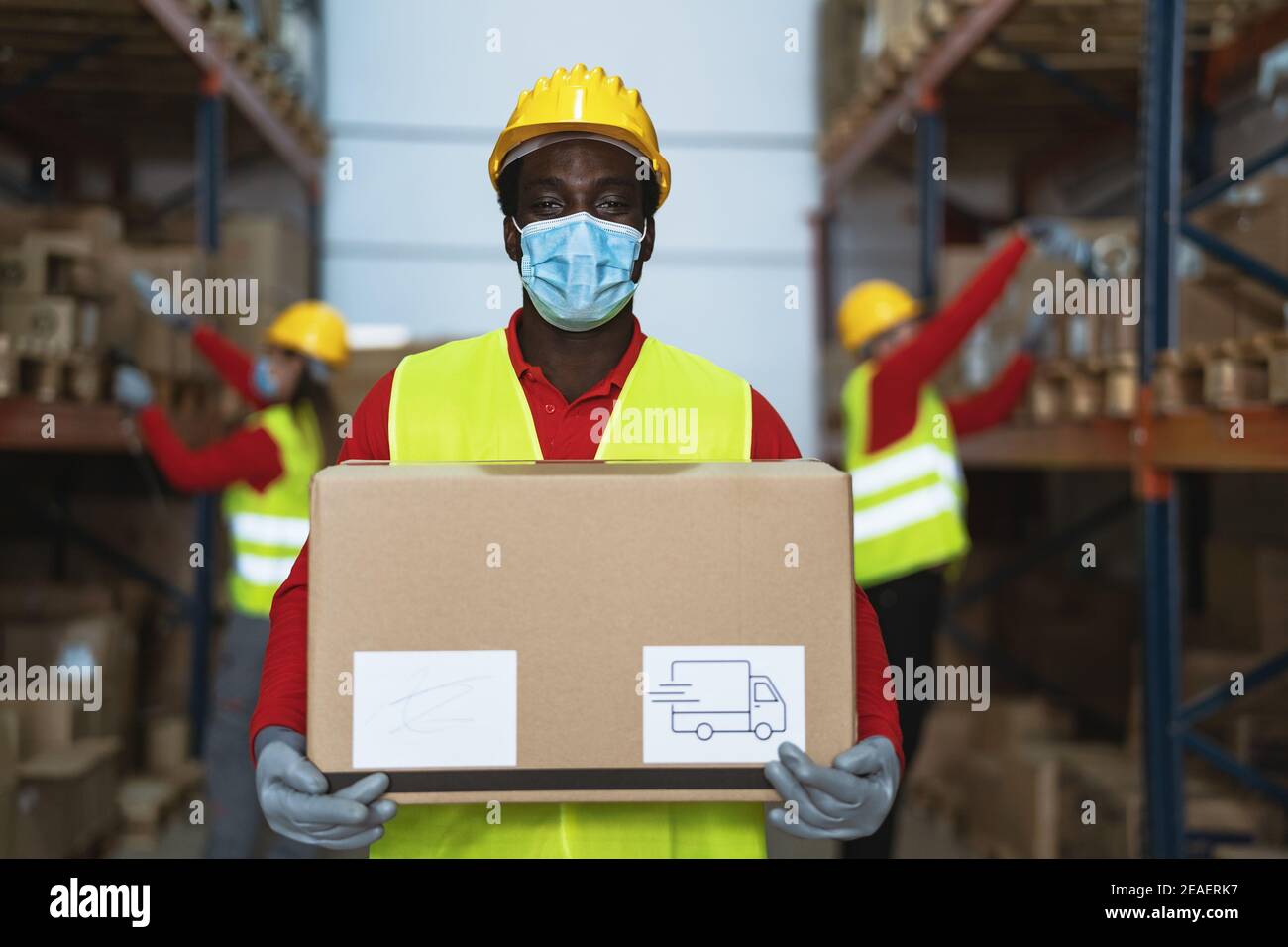 Homme noir travaillant dans l'entrepôt en chargeant les boîtes de livraison pendant le port Masque chirurgical de visage pendant la pandémie du virus corona - Logistic et concept de l'industrie Banque D'Images