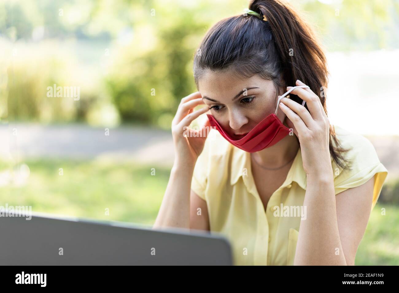 Jeune femme travaillant à l'extérieur avec un ordinateur portable et portant un visage rouge Masque pendant le temps du coronavirus - femme utilisant un masque de protection pour empêcher la propagation de Banque D'Images