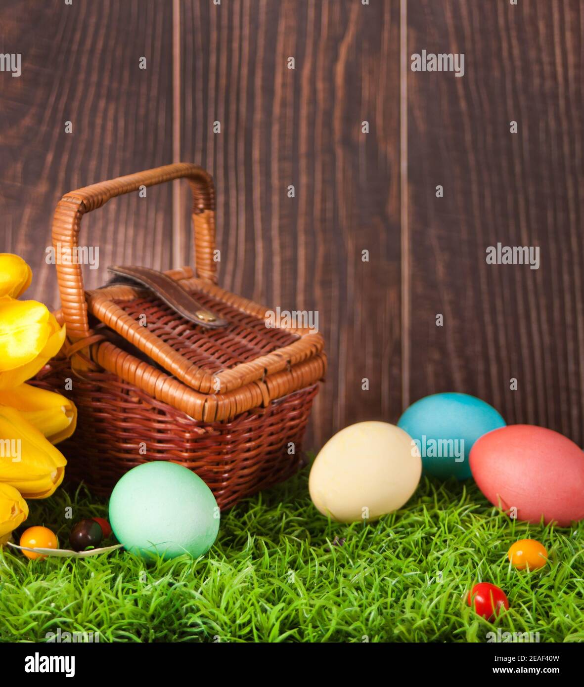 Quatre œufs de Pâques colorés décorés dans l'herbe avec des fleurs tulipes et panier de pique-nique Banque D'Images