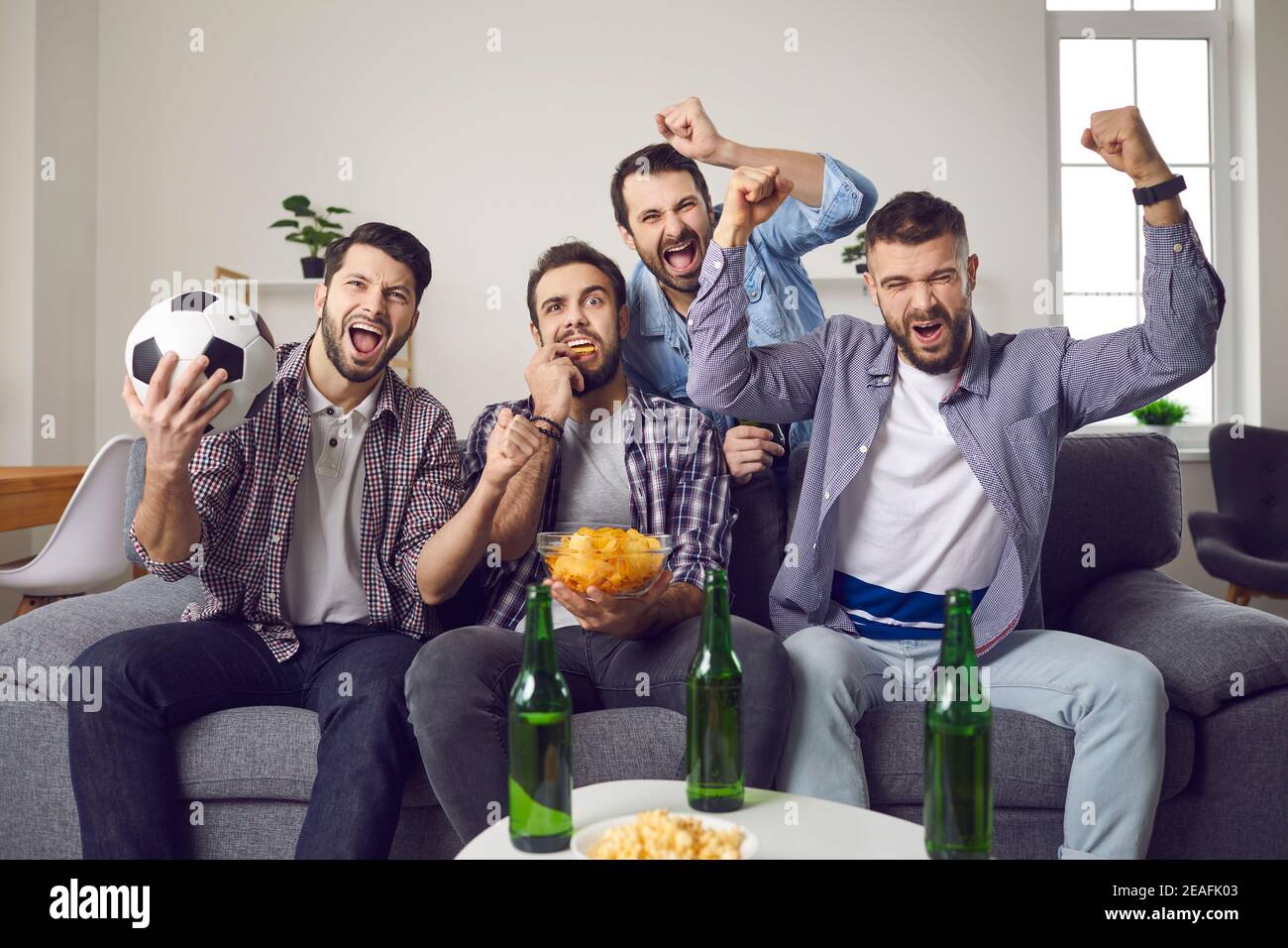 Des amis masculins célébrant le but de leurs équipes préférées lorsqu'ils regardent la télévision de football correspondance Banque D'Images