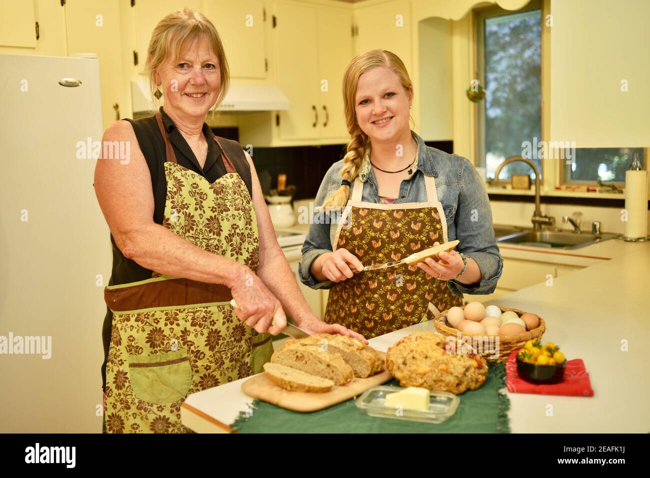Deux belles femmes caucasiennes maison boulangers en tabliers, tranchant du pain frais sur le comptoir de cuisine, buttering pain, Wisconsin, Etats-Unis Banque D'Images