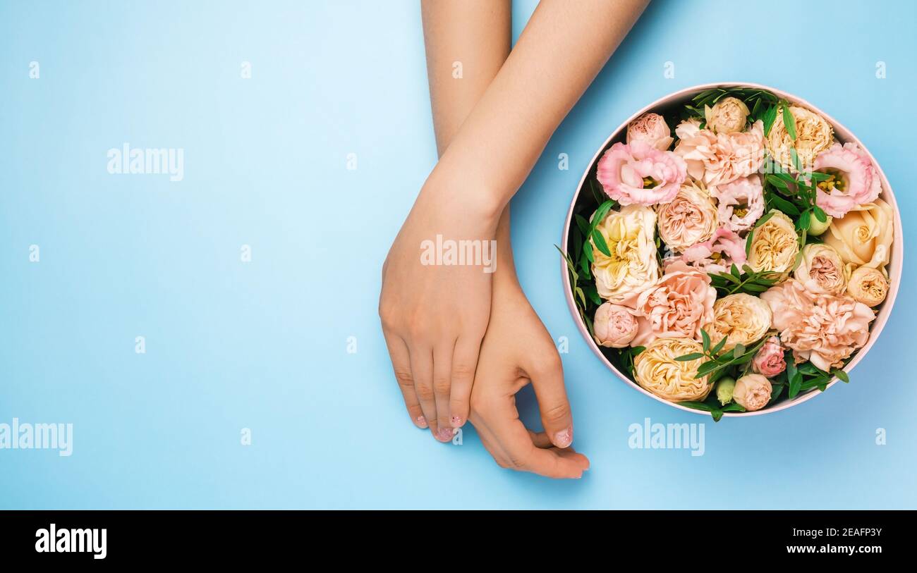Boîte avec de belles fleurs à côté des mains de womans sur le fond bleu avec espace de copie. Concept de carte salone beauté. Cadeau pour le 8 mars, Fête des mères Banque D'Images