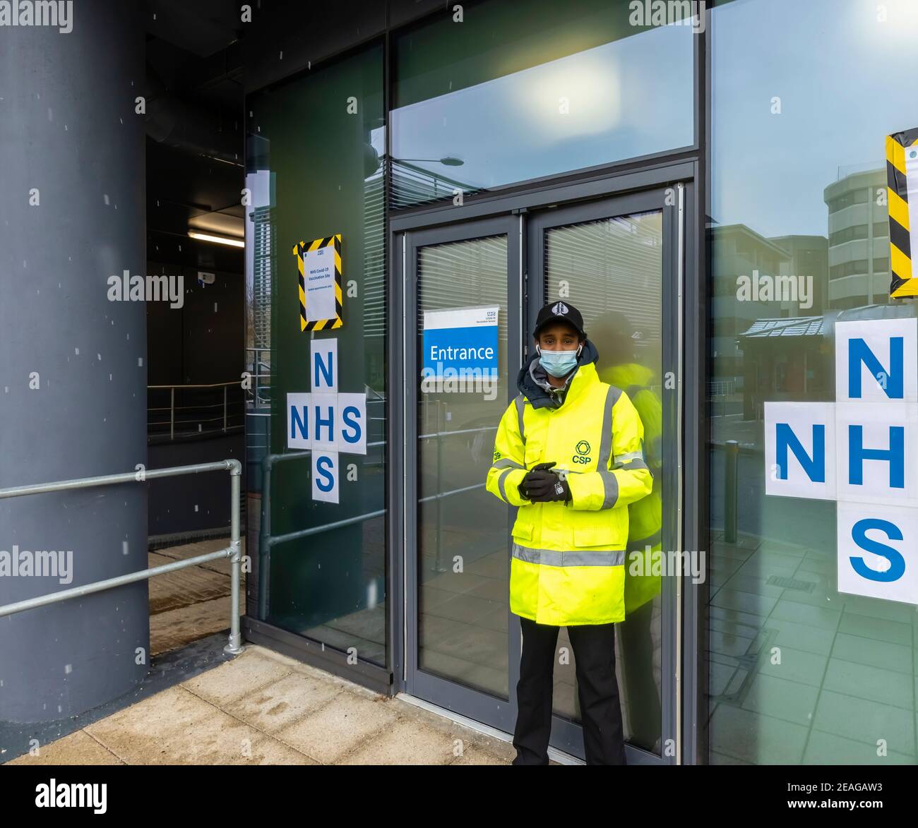 Accueillir dans une veste jaune haute visibilité devant l'entrée du site de vaccination NHS Covid-19, Victoria Gate, Chobham Road, Woking, Surrey, se, Angleterre Banque D'Images