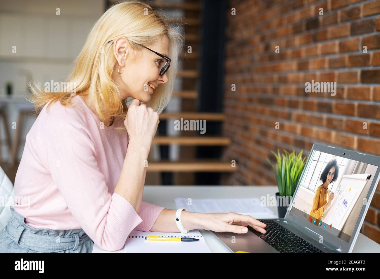 Femme d'affaires blonde mûre intelligente dans des lunettes, assise à la maison, étudiant, prenant des cours virtuels, ayant une réunion en ligne sur un ordinateur portable Banque D'Images