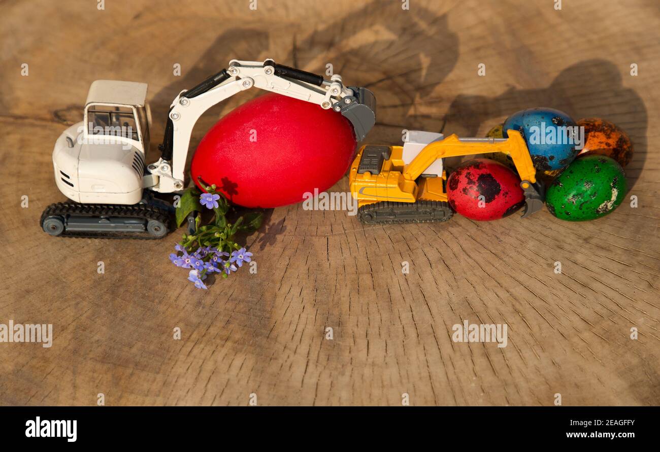 Deux modèles d'excavateurs de jouets avec des œufs de petite et de grande taille peints de couleurs vives. Concept de vacances de Pâques pour les entreprises de construction. Activité c Banque D'Images
