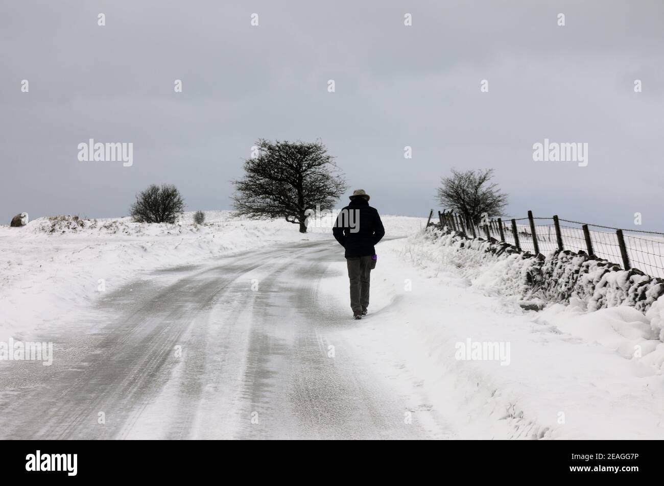 Homme marchant le long de la route enneigée à Longstone Moor Près de Bakewell dans le Peak District Banque D'Images