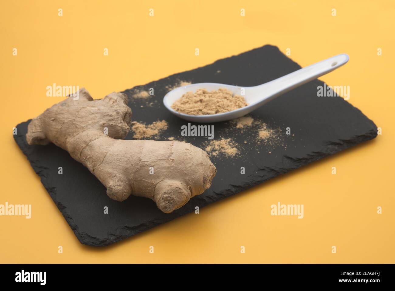 Gros plan d'une table où il y a un fragment de une racine de gingembre à côté d'une cuillère à café avec du gingembre en poudre Banque D'Images